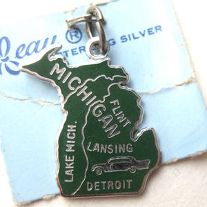 Peut inclure: Un charm en argent sterling en forme de l'État du Michigan avec un émail vert. Le bijou porte les inscriptions Michigan, Flint, Lansing, Detroit et Lake Mich., ainsi qu'un petit graphique de voiture. Il est fixé à un anneau en argent.