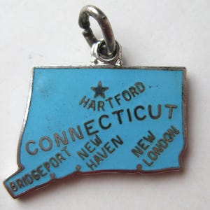 May include: A vintage charm shaped like the state of Connecticut. It has a light blue enamel surface with the state's name and cities like Hartford, Bridgeport, New Haven, and New London. The charm has a silver-tone metal border and a loop for attachment.