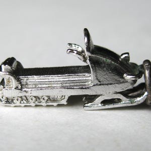 Może przedstawiać: Srebrny, miniaturowy charms w kształcie skutera śnieżnego. Charms posiada szczeg&oacute;łowe gąsienice, siedzenie, kierownicę i pętlę do przymocowania do bransoletki lub naszyjnika. Skuter śnieżny to dodatek o tematyce zimowej.