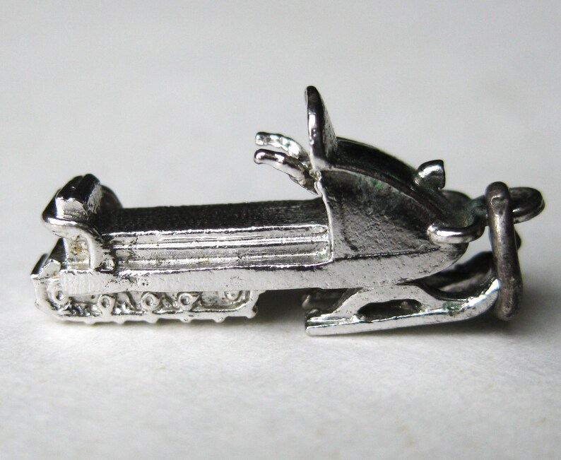 Może przedstawiać: Srebrny, miniaturowy charms w kształcie skutera śnieżnego. Charms posiada szczeg&oacute;łowe gąsienice, siedzenie, kierownicę i pętlę do przymocowania do bransoletki lub naszyjnika. Skuter śnieżny to dodatek o tematyce zimowej.