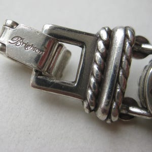 Puede incluir: Un cierre de pulsera de metal plateado con la palabra Brighton grabada en la superficie. El dise&ntilde;o del cierre incluye un marco rectangular conectado a un eslab&oacute;n texturizado de estilo cuerda trenzada con acabado met&aacute;lico pulido.