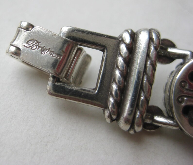 Puede incluir: Un cierre de pulsera de metal plateado con la palabra Brighton grabada en la superficie. El dise&ntilde;o del cierre incluye un marco rectangular conectado a un eslab&oacute;n texturizado de estilo cuerda trenzada con acabado met&aacute;lico pulido.