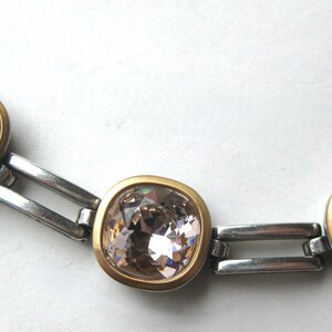 May include: A necklace featuring a series of square-shaped, light brown faceted crystals set in gold-toned bezels. The crystals are connected by polished silver-toned metal rectangular links, creating a structured chain design with a metallic finish.