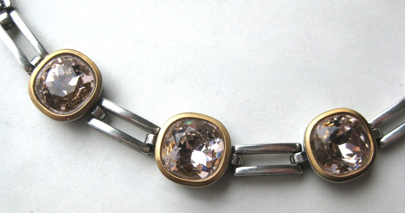May include: A necklace featuring a series of square-shaped, light brown faceted crystals set in gold-toned bezels. The crystals are connected by polished silver-toned metal rectangular links, creating a structured chain design with a metallic finish.