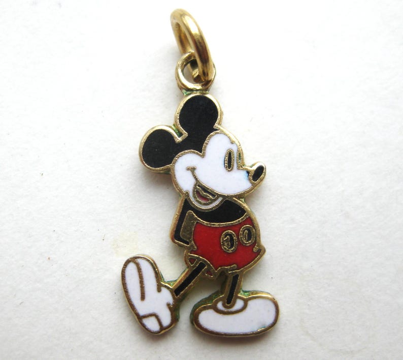 Puede incluir: Un charm dorado que representa a Mickey Mouse en un dise&ntilde;o colorido. El charm muestra a Mickey con su atuendo cl&aacute;sico: orejas negras, cara blanca, pantalones cortos rojos y zapatos amarillos. El charm est&aacute; dise&ntilde;ado con detalles de esmalte.
