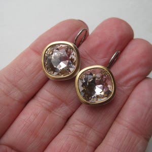 May include: A pair of earrings featuring square-cut, champagne-colored faceted crystals set in gold-toned metal bezels. Each earring includes a silver-toned metal lever-back closure, showcasing a clear, reflective surface and a polished finish.