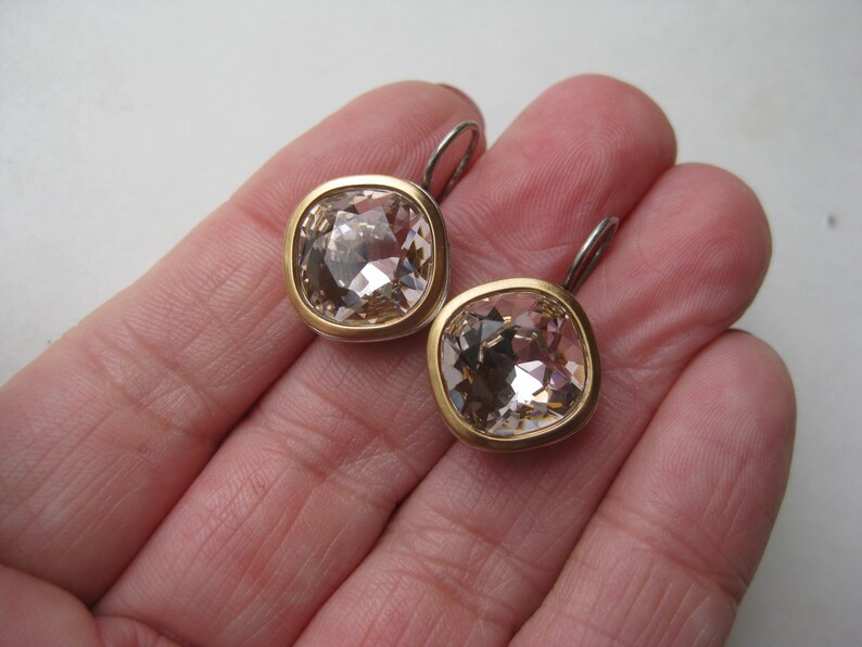 May include: A pair of earrings featuring square-cut, champagne-colored faceted crystals set in gold-toned metal bezels. Each earring includes a silver-toned metal lever-back closure, showcasing a clear, reflective surface and a polished finish.