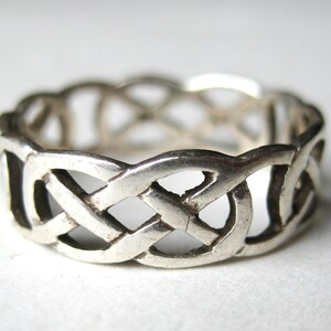 May include: A silver-toned ring featuring an openwork design of interconnected, repeating loops that form a continuous woven pattern around the entire band. The metal has a polished finish with visible depth between the intertwined segments.