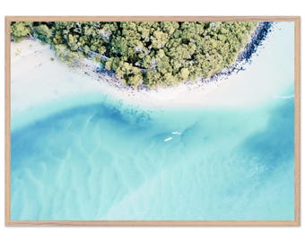 May include: Aerial view photograph of a tropical island with a sandy beach, lush green trees, and turquoise water. Two white kayaks are visible in the water. The image is framed in a light brown wooden frame.