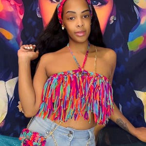 May include: A vibrant, multi-colored fringe top with a matching headband and small purse. The top and purse feature a rainbow of colors, including pink, orange, green, and blue. The outfit is paired with light blue jeans and a gold chain.