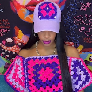 May include: A lilac baseball cap with a crocheted square design featuring pink butterflies and rhinestones. The image also shows a matching off-the-shoulder crochet top in pink, purple, and lilac colours.