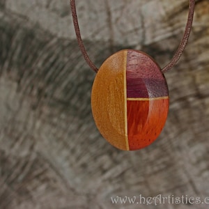 Könnte beinhalten: Ein runder Holzanhänger mit einem geometrischen Design in Braun-, Rot- und Lilatönen. Der Anhänger hängt an einer braunen Schnur.