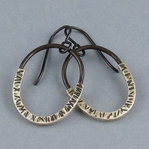 Può includere: Un paio di orecchini a cerchio in argento con una finitura testurizzata martellata. I cerchi sono attaccati a ganci per orecchini neri.