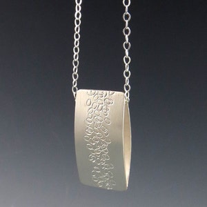 May include: A silver necklace with a rectangular pendant featuring a textured design of small circles.