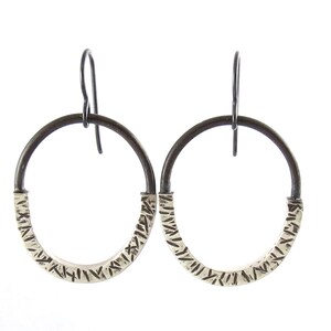 Può includere: Un paio di orecchini a cerchio in argento con un design testurizzato. I cerchi sono in argento ossidato e hanno una finitura nera.