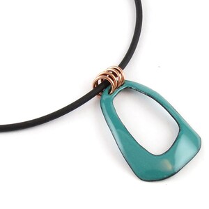 Può includere: Collana con pendente turchese dalla forma geometrica. Il pendente è attaccato a un cordino nero e rifinito con anelli in metallo color rame. La collana è presentata su sfondo bianco.