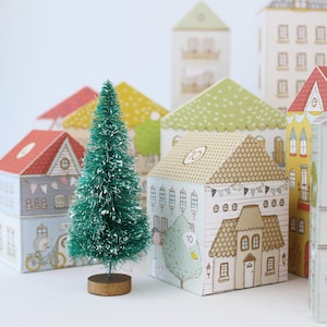 Several printable advent calendar houses next to a bottle brush tree