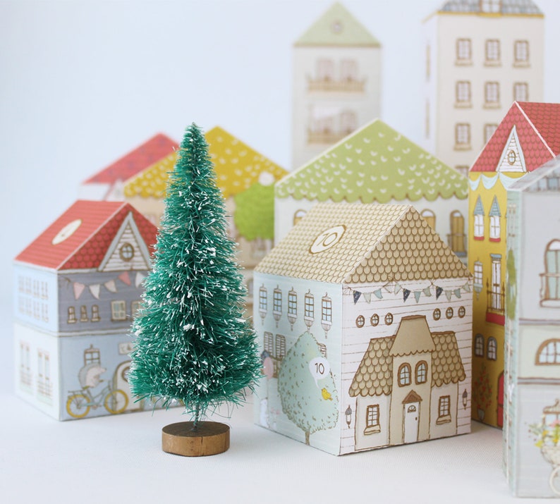 Several printable advent calendar houses next to a bottle brush tree