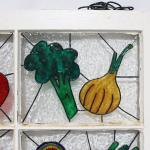 May include: A white windowpane with a stained glass design featuring a green broccoli, a yellow onion, and a red tomato. The windowpane is set in a white wooden frame.