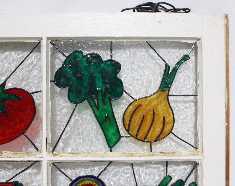 May include: A white windowpane with a stained glass design featuring a green broccoli, a yellow onion, and a red tomato. The windowpane is set in a white wooden frame.
