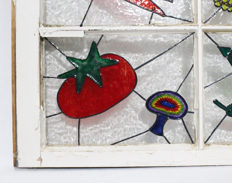 May include: A stained glass window pane featuring a red tomato, a green leaf, and a colourful mushroom. The window pane is set in a white wooden frame.