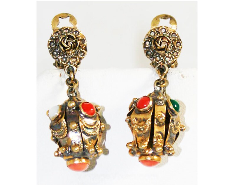 Puede incluir: Un par de pendientes colgantes de tono dorado con un dise&ntilde;o floral en la parte superior y un racimo de piedras redondas multicolores en la parte inferior.