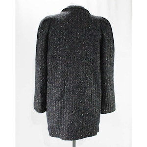 May include: A dark gray tweed jacket with a textured pattern. The jacket has a long sleeve and a button closure.