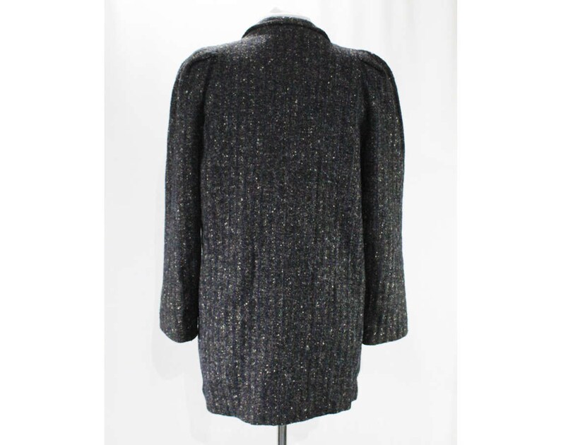 May include: A dark gray tweed jacket with a textured pattern. The jacket has a long sleeve and a button closure.
