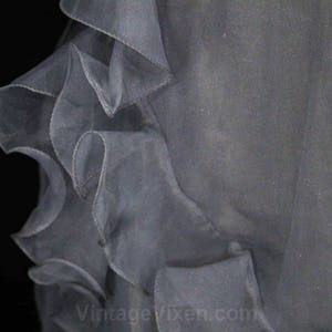 May include: A close-up of a gray tulle fabric with ruffled edges. The fabric is soft and sheer, and the ruffles are delicate and flowing.