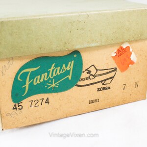 May include: A vintage shoe box with a green and gold label that says "Fantasy" and a picture of a brown shoe. The box is labeled with the numbers "45 7274" and "7 N".