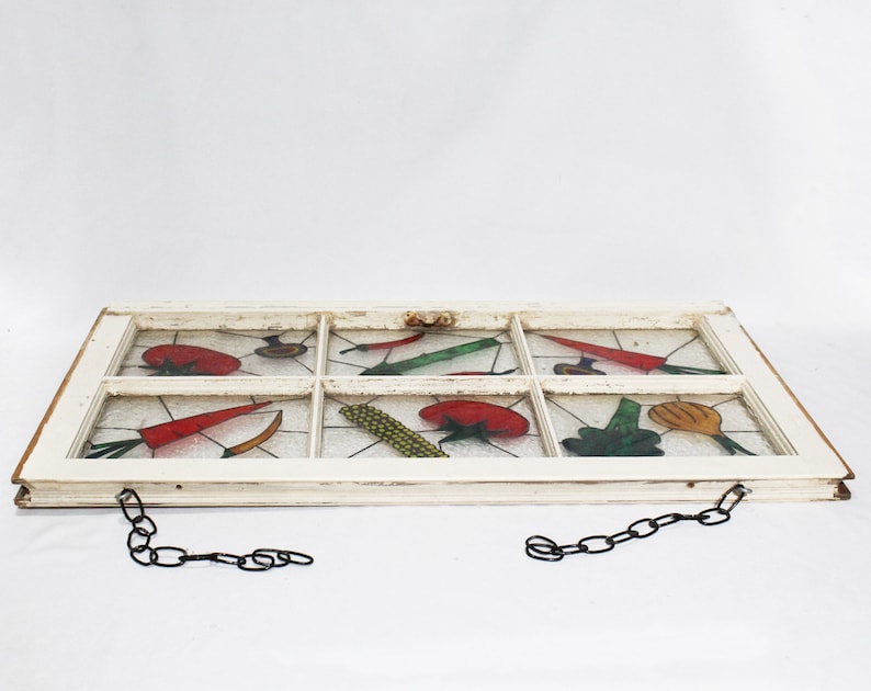 May include: A white painted window frame with a chain hanging from each side. The glass panes are painted with colourful vegetables, including tomatoes, carrots, corn, and peppers.