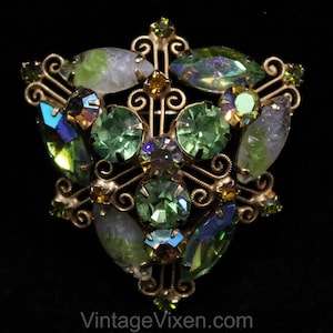 May include: A vintage brooch with a gold tone metal setting and a variety of green, blue, and clear rhinestones. The brooch is in the shape of a starburst.