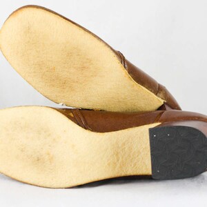 May include: Brown leather heeled boots with a rubber sole. The boots have a brown leather upper and a rubber sole. The boots are shown from the bottom, with the soles facing the camera.