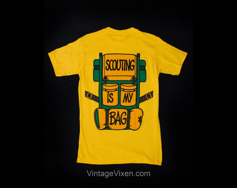 Puede incluir: Camiseta amarilla con una ilustraci&oacute;n verde y naranja de una mochila con el texto "SCOUTING IS MY BAG" en la parte posterior.