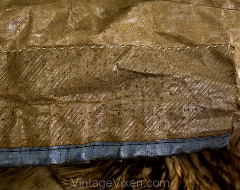 May include: Close-up of a section of vintage brown fabric with a textured, woven pattern. The fabric is stitched with white thread in a horizontal line. The bottom edge is trimmed with a dark grey material.