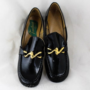 May include: Pair of black patent leather loafers with gold buckle accents. The loafers have a pointed toe and a low heel. The brand name "Fantasy" is visible on the insole.
