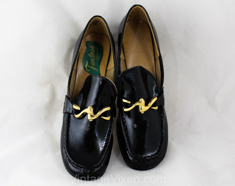 May include: Pair of black patent leather loafers with gold buckle accents. The loafers have a pointed toe and a low heel. The brand name "Fantasy" is visible on the insole.