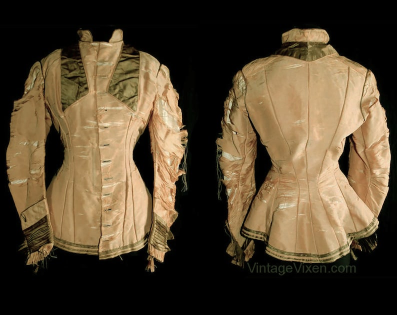 May include: A vintage light pink jacket with a high collar and long sleeves. The jacket features a fitted waist, decorative trim, and a row of buttons down the front. The sleeves have a unique, layered design. The jacket is displayed against a black background.