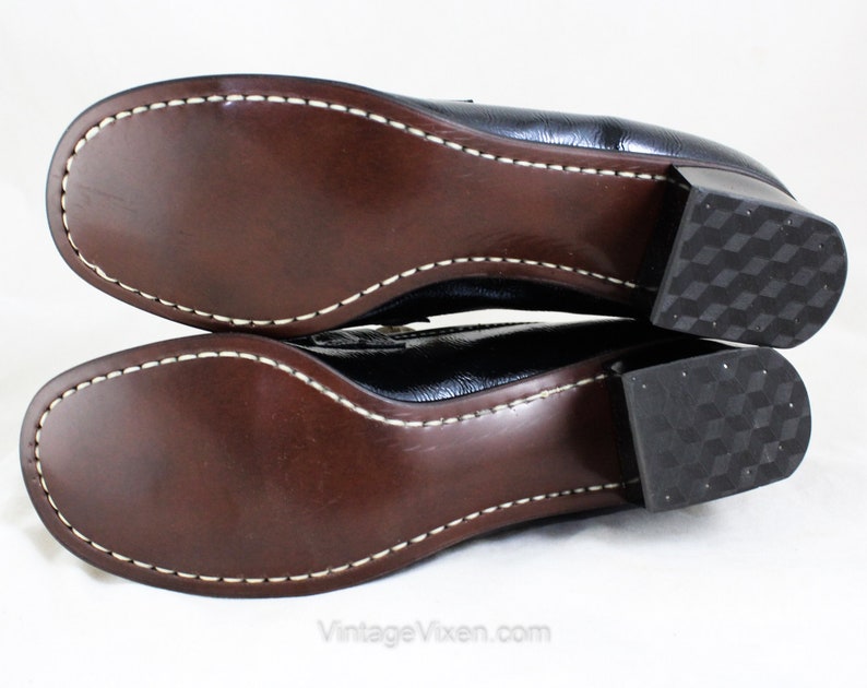 May include: A pair of black leather heeled shoes with a brown leather sole and a white stitch detail around the edge. The heels are block heels with a textured pattern.