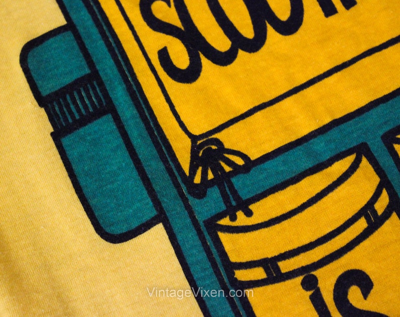Puede incluir: Camiseta amarilla con un gr&aacute;fico negro y verde azulado de una mochila con el texto "School is"