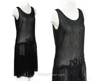 May include: A black beaded flapper dress with a scoop neck and a beaded embellishment at the waist. The dress has a sheer, flowing skirt.
