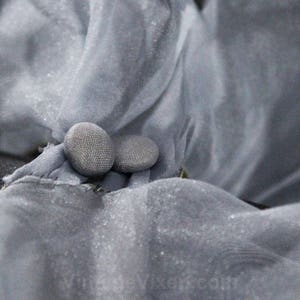May include: Two gray buttons sewn onto a piece of gray fabric.