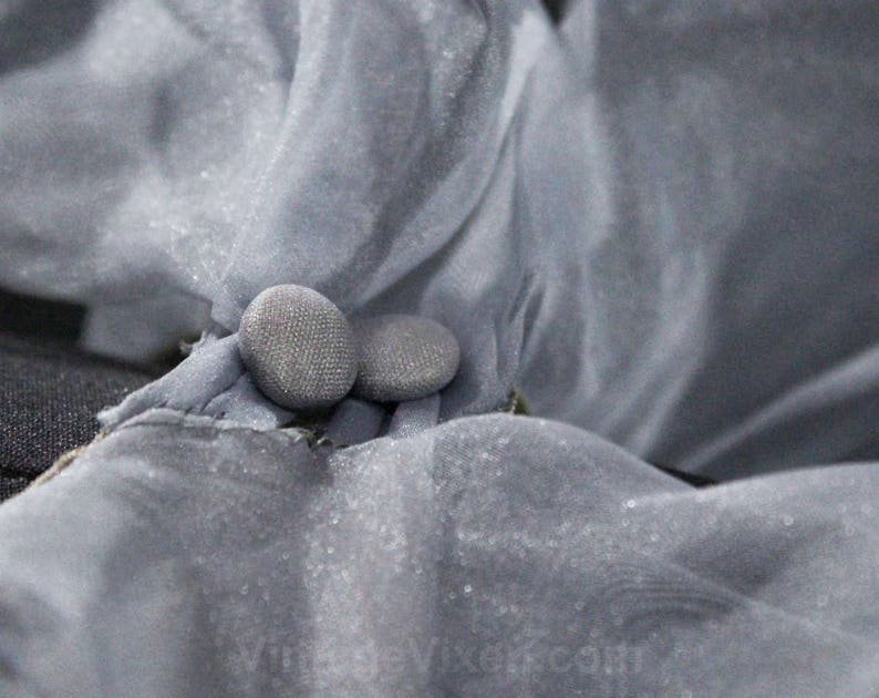 May include: Two gray buttons sewn onto a piece of gray fabric.