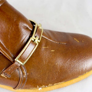 May include: Brown leather slip-on shoe with a gold buckle strap.