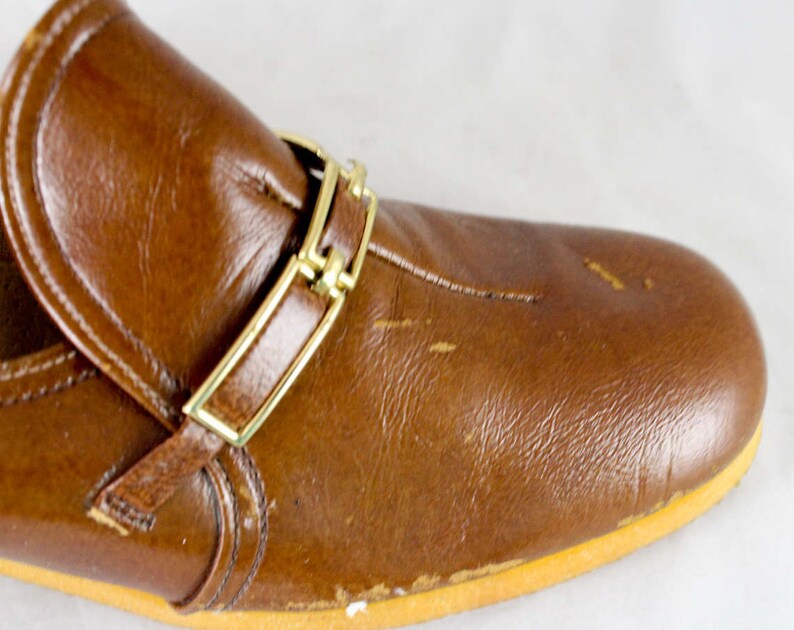 May include: Brown leather slip-on shoe with a gold buckle strap.