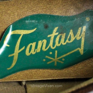 May include: Close-up of a green label with the word "Fantasy" in gold lettering and a gold star design. The label is attached to a brown leather surface.