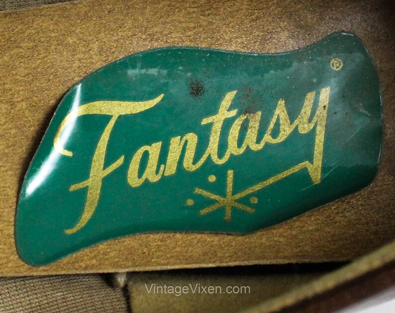 May include: Close-up of a green label with the word "Fantasy" in gold lettering and a gold star design. The label is attached to a brown leather surface.