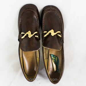 May include: A pair of brown leather loafers with gold buckles. The loafers have a pointed toe and a low heel. The brand name "Hush Puppies" is visible on the insole of one shoe.
