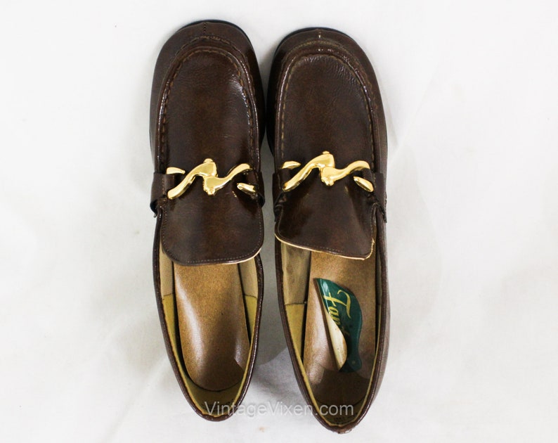 May include: A pair of brown leather loafers with gold buckles. The loafers have a pointed toe and a low heel. The brand name "Hush Puppies" is visible on the insole of one shoe.