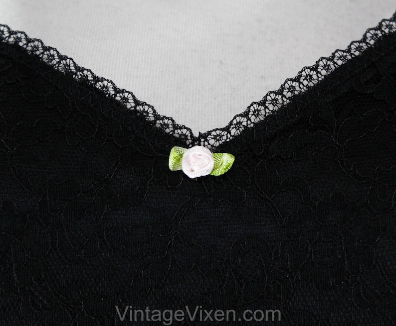 May include: Black lace fabric with a small pink and green flower embellishment.